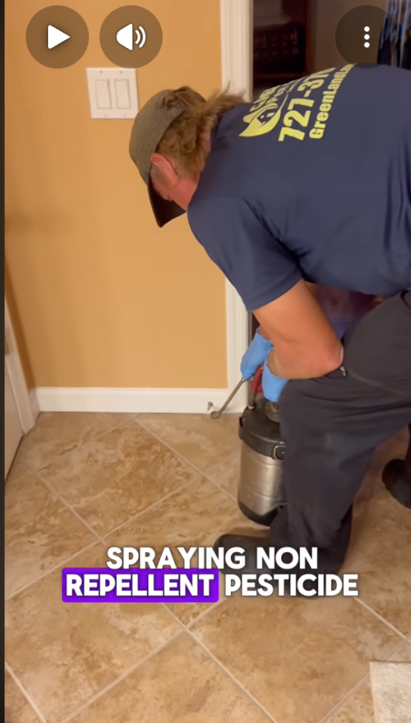 A man with a pesticide sprayer spraying a baseboard of a wall