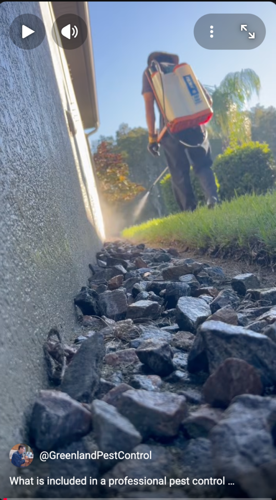 A house with a rock bed along it and a man spraying the house with a backpack sprayer