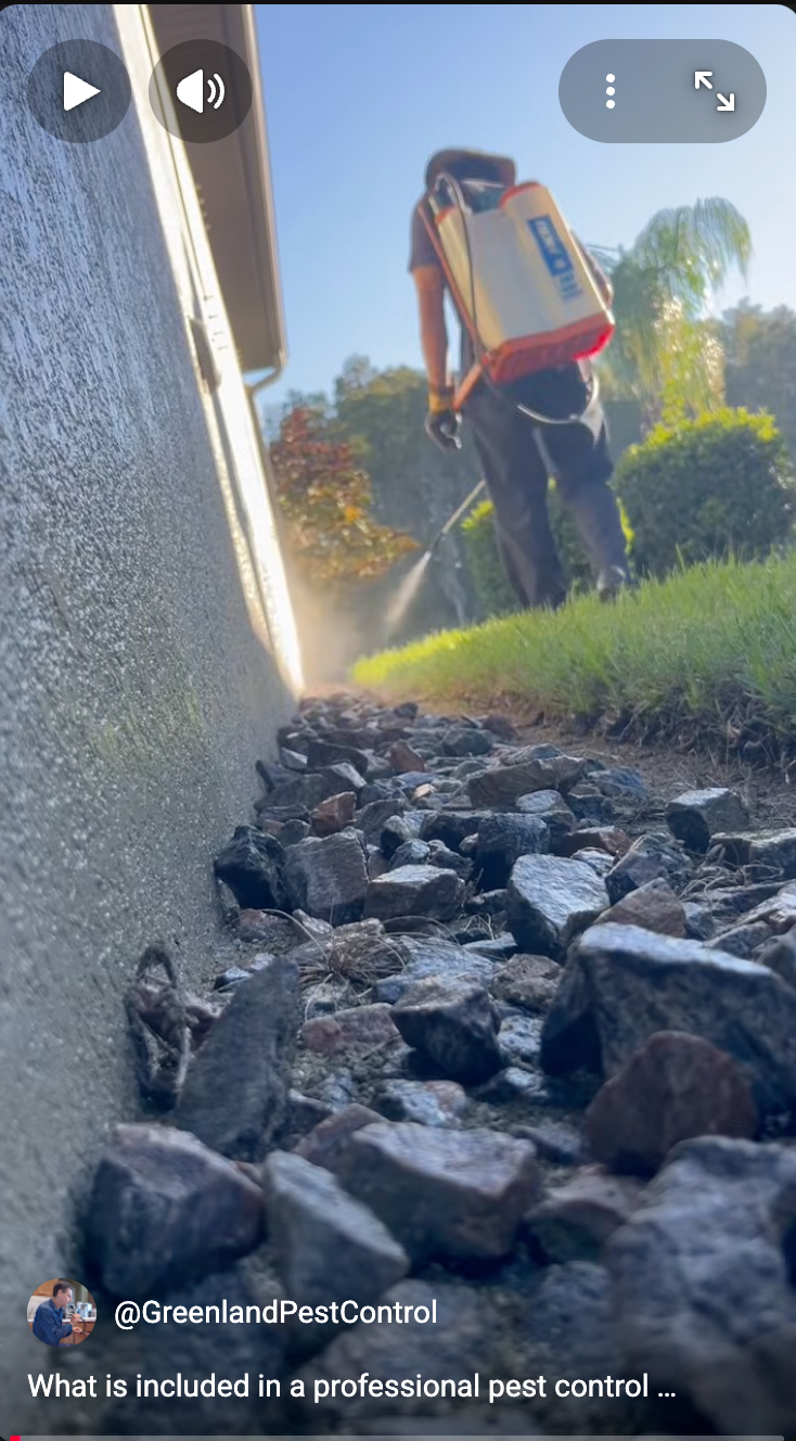 A house with a rock bed along it and a man spraying the house with a backpack sprayer